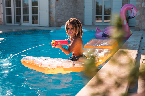 A happy young boy floating on a pool toy, and having a blast with a squirt gun at the villa pool.