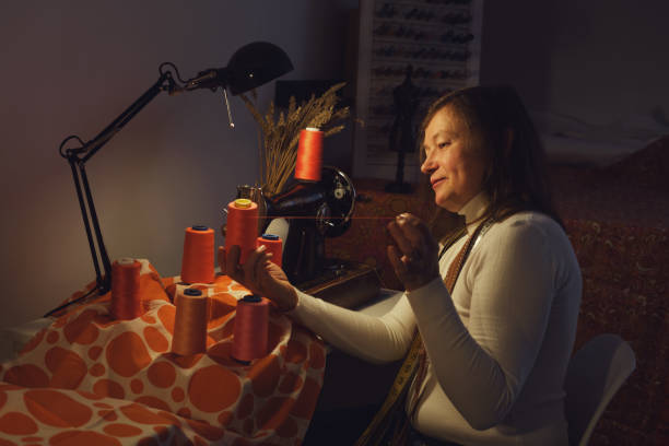 Woman working in her sewing studio at night, she is sitting on the sofa and working with a sewing machine