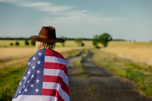 Woman in USA flag and hat on country road