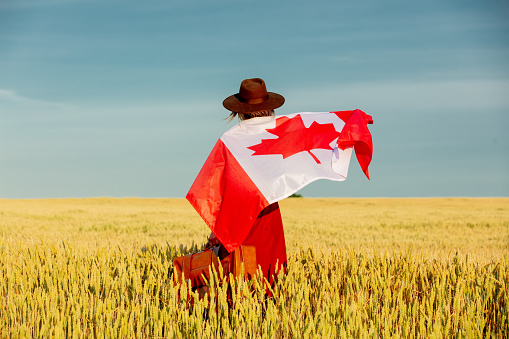 Girl with Canada flag in wheat field and blue sky on background