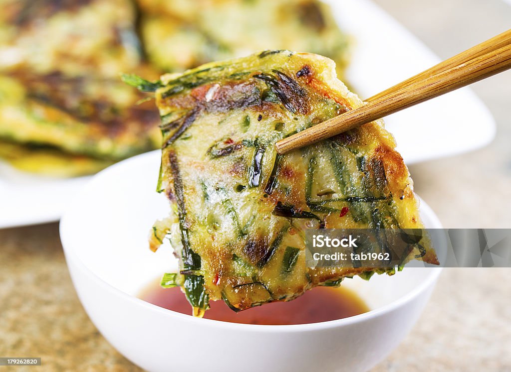 Korean Green Onion Pancakes Ready to Eat Horizontal photo of Korean Green Onion Pancake being held with chopsticks while be dipped into small cup of sauce in front of plate filled with more pancakes Bowl Stock Photo