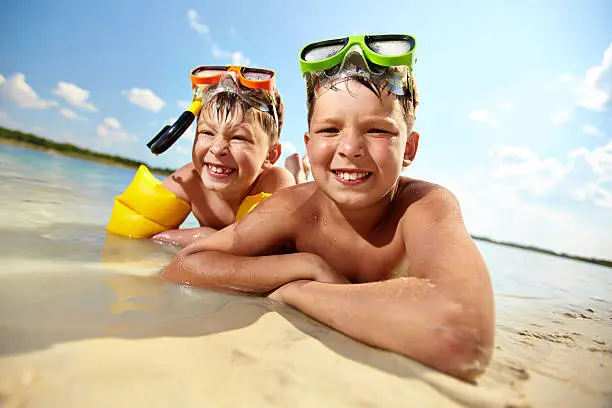 Photo of happy siblings lying on sand on summer vacation
