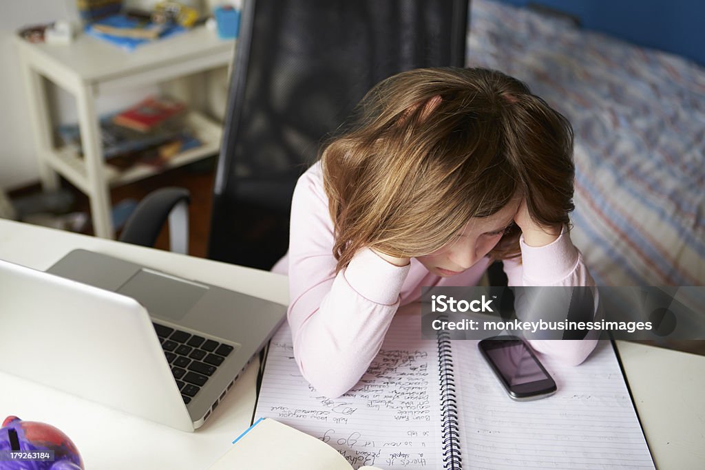 Girl using smartphone and laptop to study in bedroom Girl Using Mobile Phone Instead Of Studying In Bedroom Sitting In Chair With Head In Hands Child Stock Photo