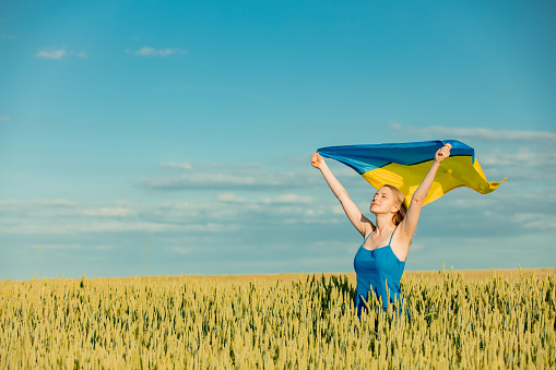 Girl with Ukrainian flag in wheat field