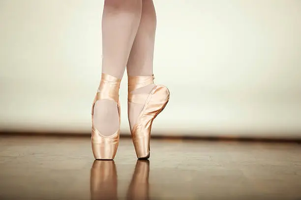 Young ballerina dancing, closeup on legs and shoes, standing in pointe position.