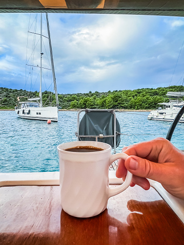 Men crew member holding coffee mug on sailboat in early morning. Model released.