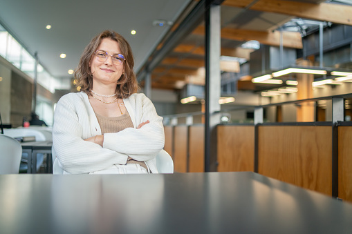 A young female student sits across the table with her arms crossed looking at camera