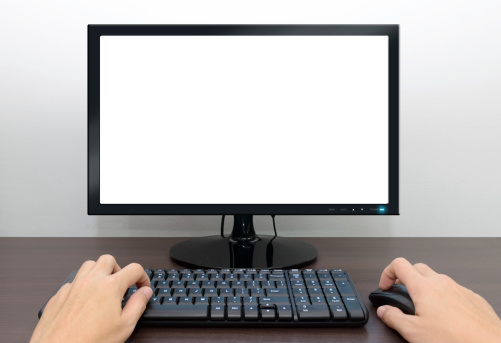 Closeup image of blank monitor and male hands over the computer keyboard and mouse