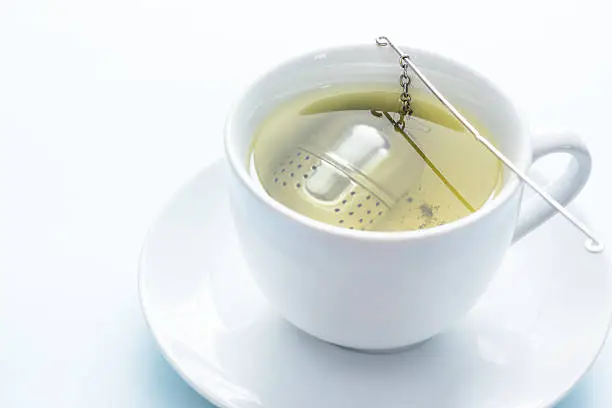 A white cup of green tea with an infuser (tea ball)