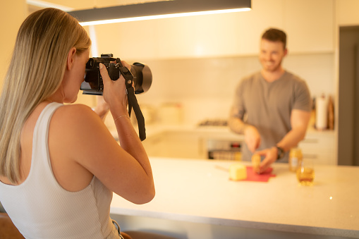 A young female photographer takes photo of male cooking