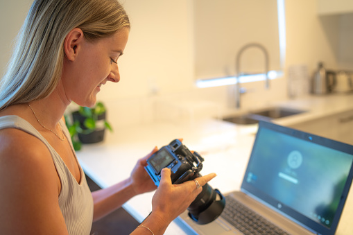 A female photographer looks at photos on her camera while laptop loads