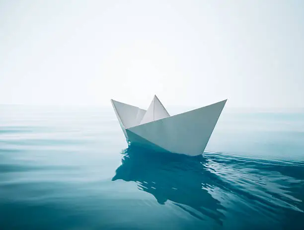 paper boat sailing on water causing waves and ripples