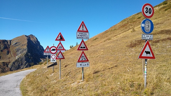 Twelve different road signs at start of downhill small mountain road in Italy