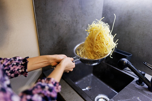 Two teenage kids preparing spaghetti dinner in the kitchen. Teenage girl has drained the pasta and is tossing the spaghetti on a colander
Canon R5