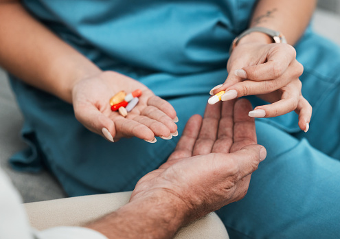 Pills, senior medication and man hands with a nurse and caregiver giving medicine at clinic. Retirement, nursing home and care of a healthcare, wellness and hospital worker with prescription drugs