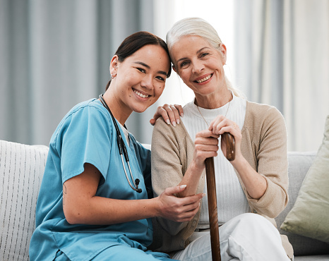 Nurse, elderly woman and sofa for portrait, walking stick and smile together with happiness, chat and care. Elderly patient, asian doctor and couch with helping hand, happy and connection for support
