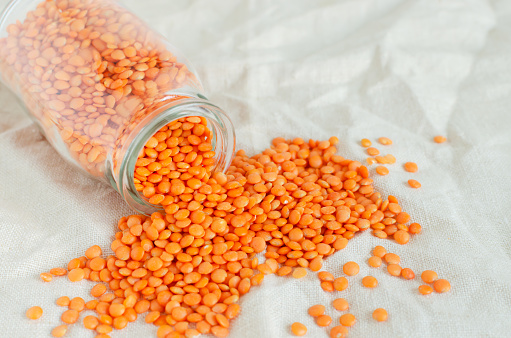 Orange lentils in a glass jar on a linen tablecloth. The concept of proper nutrition. Vegan and vegetarian food. Horizontal orientation. Copy space