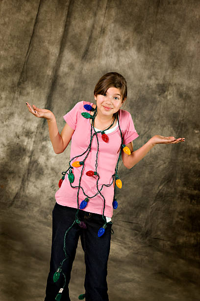 Beautiful Young Girl Frustrated and Tangled in Christmas Lights Beautiful young girl holds up her hands in frustration as she's tangled in Christmas lights. christmas chaos stock pictures, royalty-free photos & images