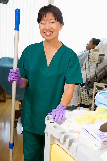 An Orderly Mopping The Floor In A Hospital Ward An Orderly Mopping The Floor In A Hospital Ward Smiling At Camera With Patient Lying In Bed In Background personal care aid stock pictures, royalty-free photos & images