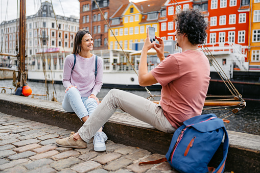 Boyfriend taking pictures of his girlfriend using a smart phone in Nyhavn Canal in Copenhagen in Denmark.
