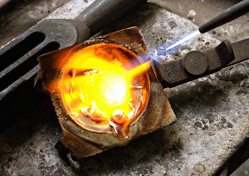 Artisanal jeweler heats pure silver in a crucible on her workbench before casting a piece of jewelry