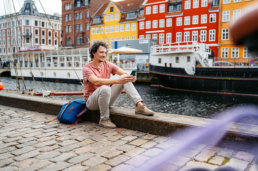 Handsome young man using his smart phone in Nyhavn Canal in Copenhagen in Denmark.
