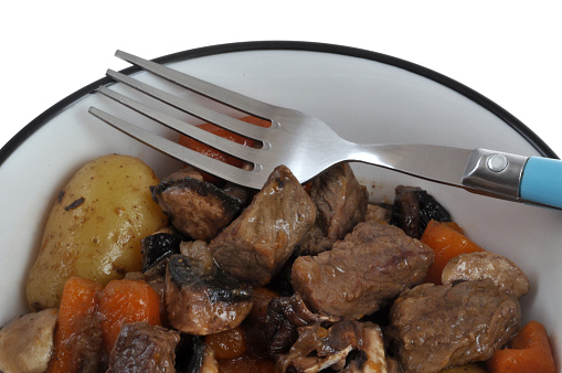 Plate of pot-au-feu with a fork close-up on white background