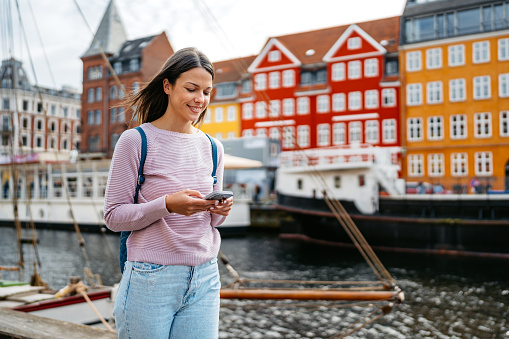 Beautiful young woman using her smart phone in Nyhavn Canal in Copenhagen in Denmark.