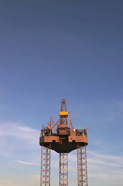 "An oilrig against a blue sky, some clouds."