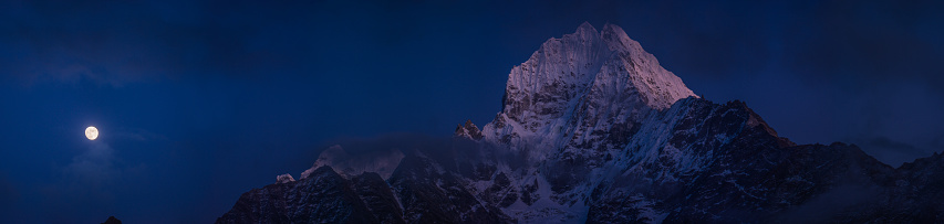 The snow capped peaks of Thamserku 6608m and Kangtega 6782m illuminated by the rising moon high in the Himalayan mountain wilderness of the Sagarmatha National Park, Nepal.