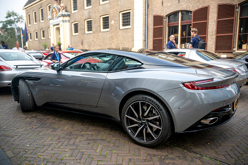 Aston Martin DB11 sports car in grey in the streets of Zwolle with people looking at the car. The Aston Martin DB11 is a luxury grand tourer unveiled in 2016 and available with V8 and V12 petrol engines.