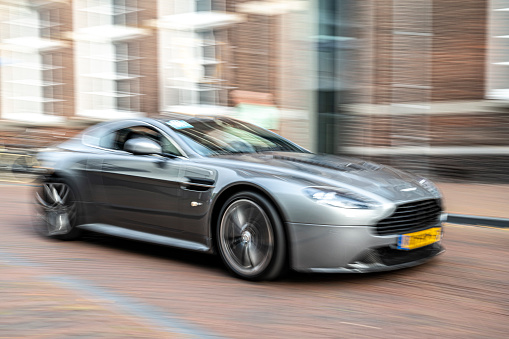 Aston Martin V12 Vantage coupe sports car driving on a street in the city of Zwolle. The Aston Martin V12 Vantage is a high-performance sports car with front-mounted 6.0-liter V12 engine.