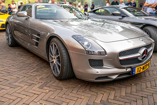 Mercedes-AMG SLS sports car parked in a square in the city of Zwolle during a sunny summer morning. People in the background are looking at the cars.