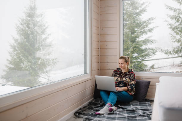 Female remote work on laptop in front of panoramic window with great view of mountain. Remote work from cozy place. Workplace in house in snowy morning. Wide interior view. Concept freelance lifestyle trabajo remoto femenino en computadora portátil frente a una ventana panorámica con una gran vista de la montaña. trabajo remoto desde un lugar acogedor. lugar de trabajo en casa en la mañana nevada. amplia vista interior. concepto de estilo de vida fr