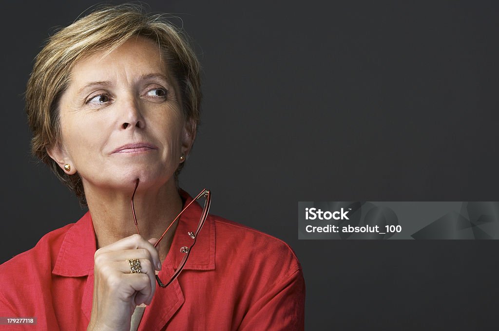 A middle aged woman thinking with her glasses in her hand Mid adult woman holding glasses and looking sidewards Contemplation Stock Photo