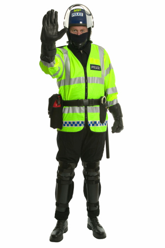 Policeman in riot gear and hi-vis jacket gesturing for you to stop.