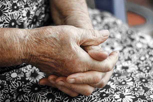 Choose up of old woman clasping hands together in lap stock photo