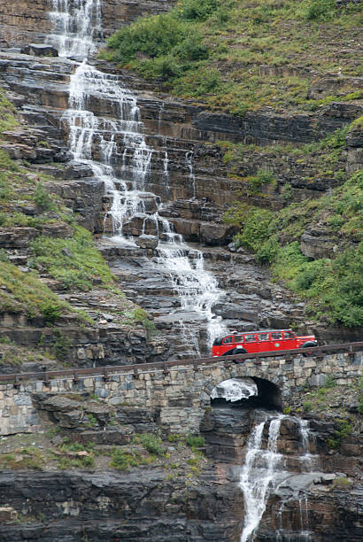 red bus passant une cascade dans le parc national de glacier, montana - us glacier national park montana bus park photos et images de collection