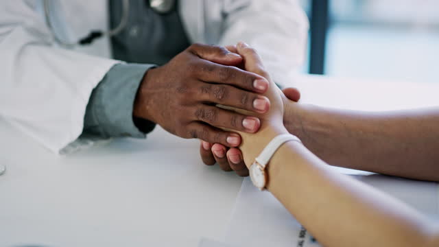 Holding hands, doctor or patient on desk for support, cancer diagnosis or comfort in hospital. People, trust or consultation with care or empathy, wellness or medical advice in clinic for healthcare
