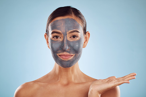 Face mask, skincare and beauty of woman showing product for facial treatment isolated in a blue studio background. Skin, charcoal and young female person with clean, hydration and dermatology cream