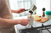 Pouring hot tasty black coffee from cezve for breakfast at kitchen at home