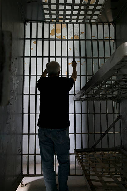 istock Man behind bars in a prison cell facing a wall 179282239