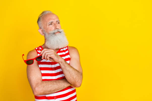 istock Photo of thoughtful old gray haired man taking off sunglass when looking empty space summer cocktails isolated on yellow color background 1792829182