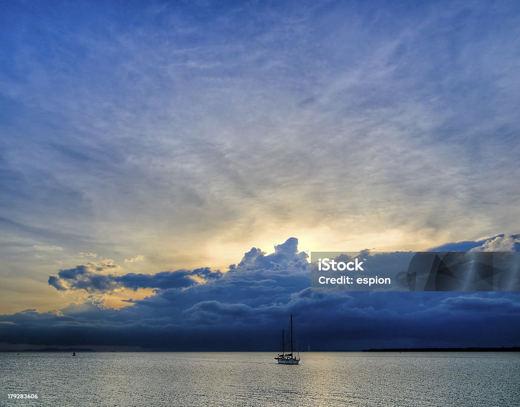 Distant Storm Yacht returning to moor as a tropical convectional storm rages in the distant at sunset Arrival Stock Photo