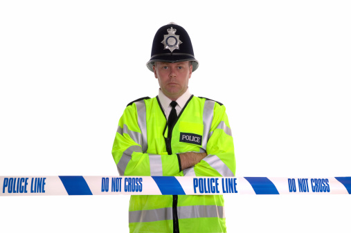 British Police officer standing behind some cordon tape. Focus is on the tape.