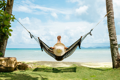 Summer vacations concept. Happy woman in black bikini relaxing in hammock on tropical beach