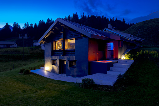 Modern forest house equipped with solar panels and an energy storage wall battery during dusk.