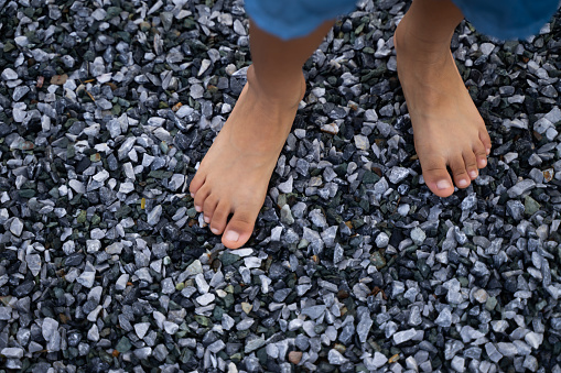 The feet of a dark-skinned boy stand on a small cobblestone floor, barefoot without shoes.