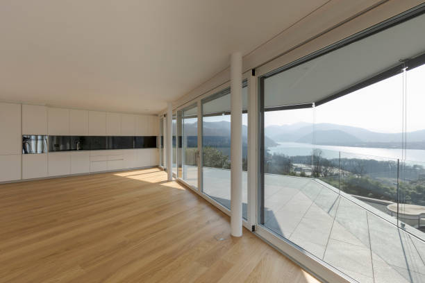 istock Modern living room with open space and a black and white designed kitchen situated at the end. Large windows allow plenty of sunlight to enter. 1792893767