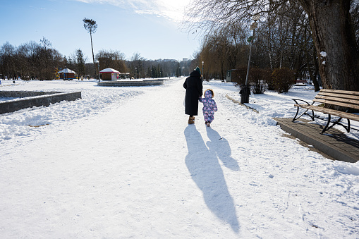 Back view of mother and child walking on a sunny frosty winter day in the park.